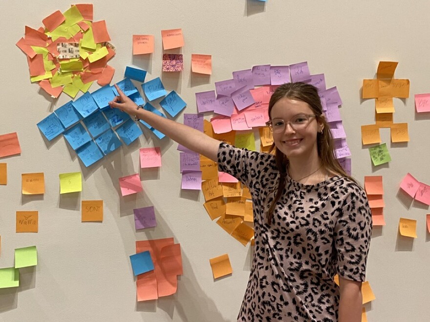 Evelyn Elliott points to the brainstorming wall where campers posted their ideas for the Create and Curate Showcase.