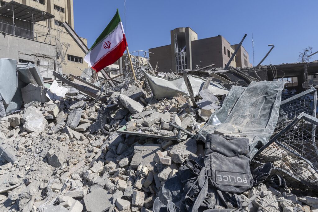 An Iranian flag is planted in the rubble of a police station, damaged in airstrikes on March 3, 2026, in Tehran. The United States and Israel have continued the joint attack on Iran that began on Feb. 28. Iran retaliated by firing waves of missiles and drones at Israel, and targeting U.S. allies in the region. (Photo by Majid Saeedi/Getty Images)