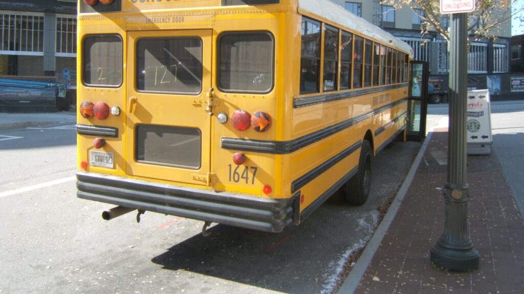 Rear view of a yellow school bus parked along a city street curb with its front door open.
